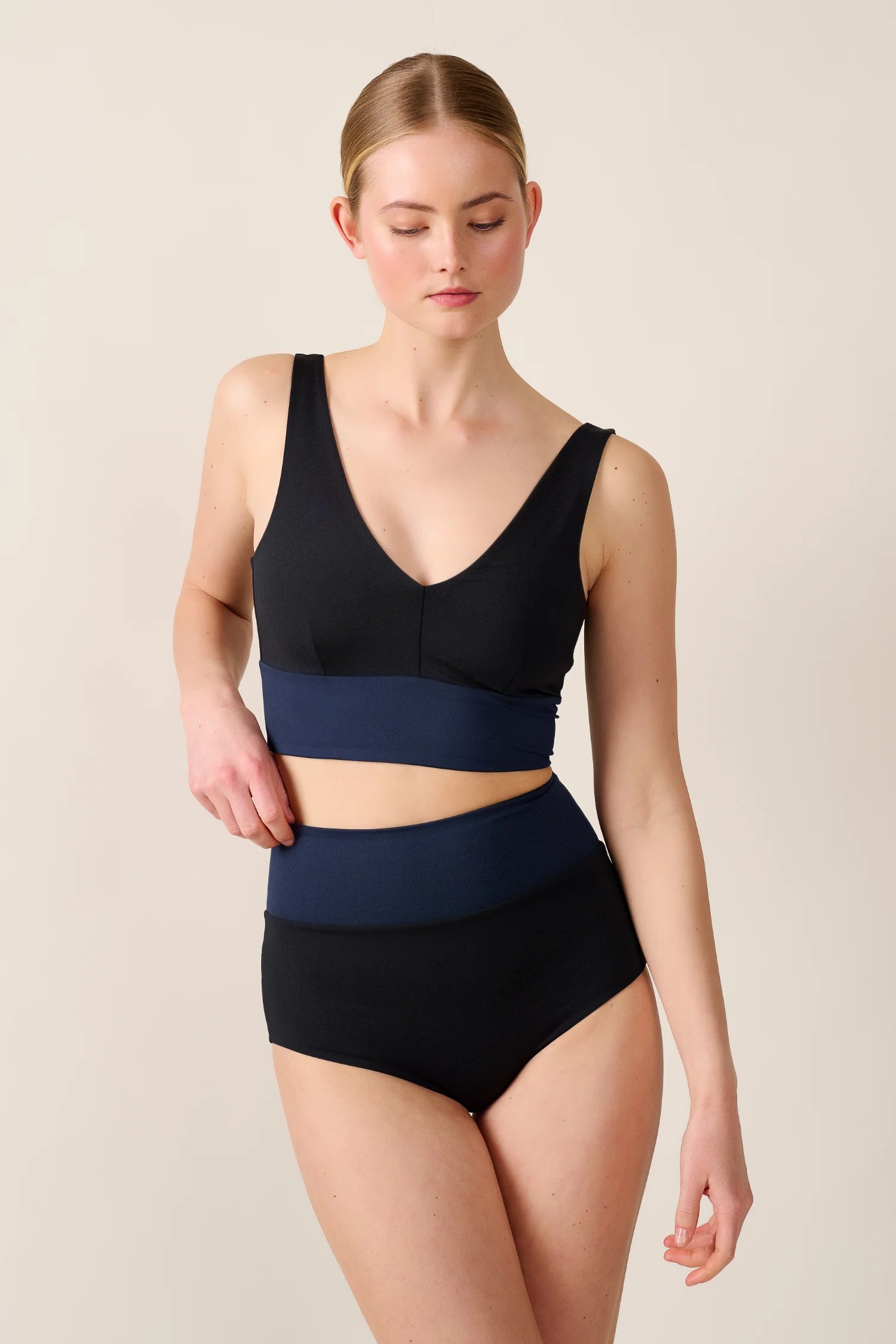 Frau trägt MYMARINI Bikinitop mit V-Ausschnitt und High-Waist-Bikinihose in Schwarz und Blau.#color_black-navy