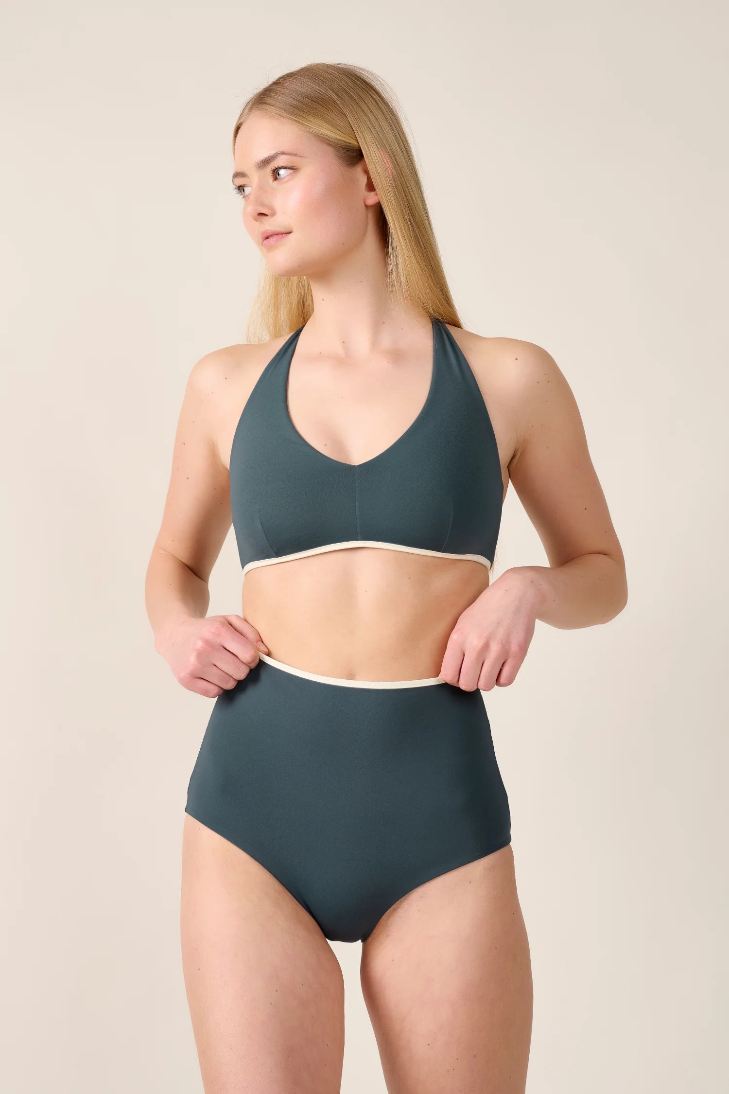 Frau trägt MYMARINI Bikini mit V-Ausschnitt und High Waist in Dunkelgrün, schaut nach links vor neutralem Hintergrund.#color_black-grey-white