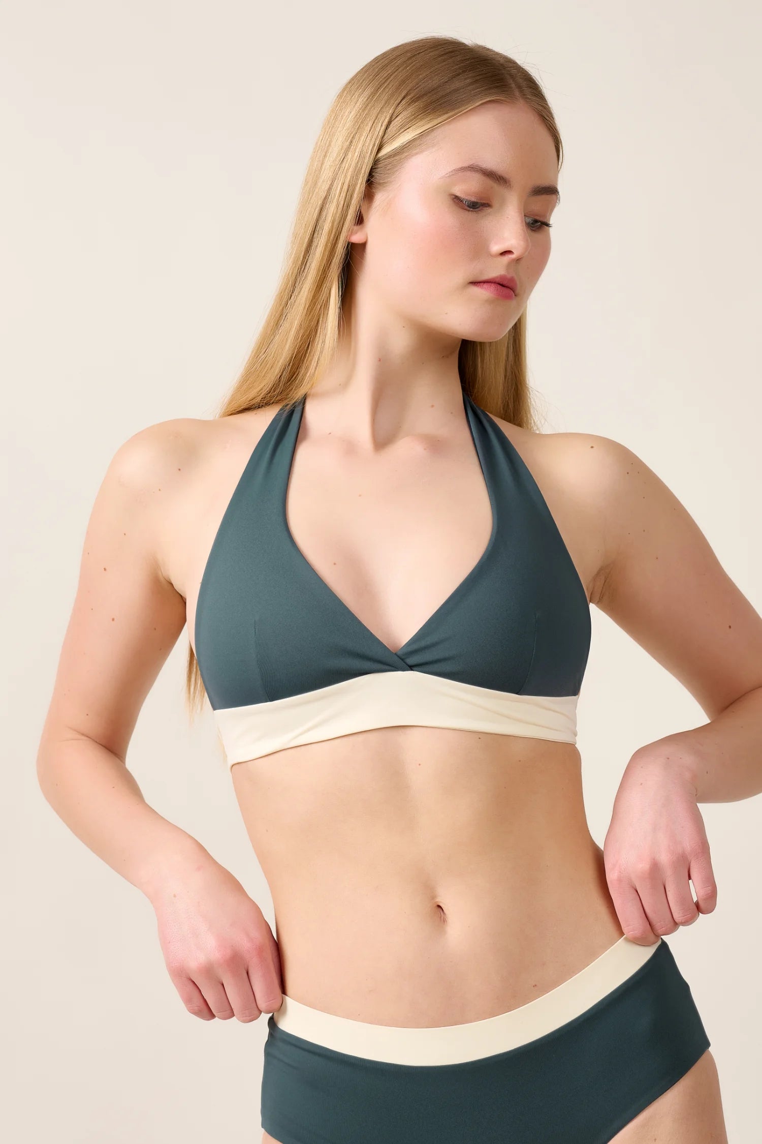 Frau trägt MYMARINI Neckholder-Bikinitop und Bikinihose in Dunkelgrün mit cremefarbenem Bund vor neutralem Hintergrund.#color_black-grey-white
