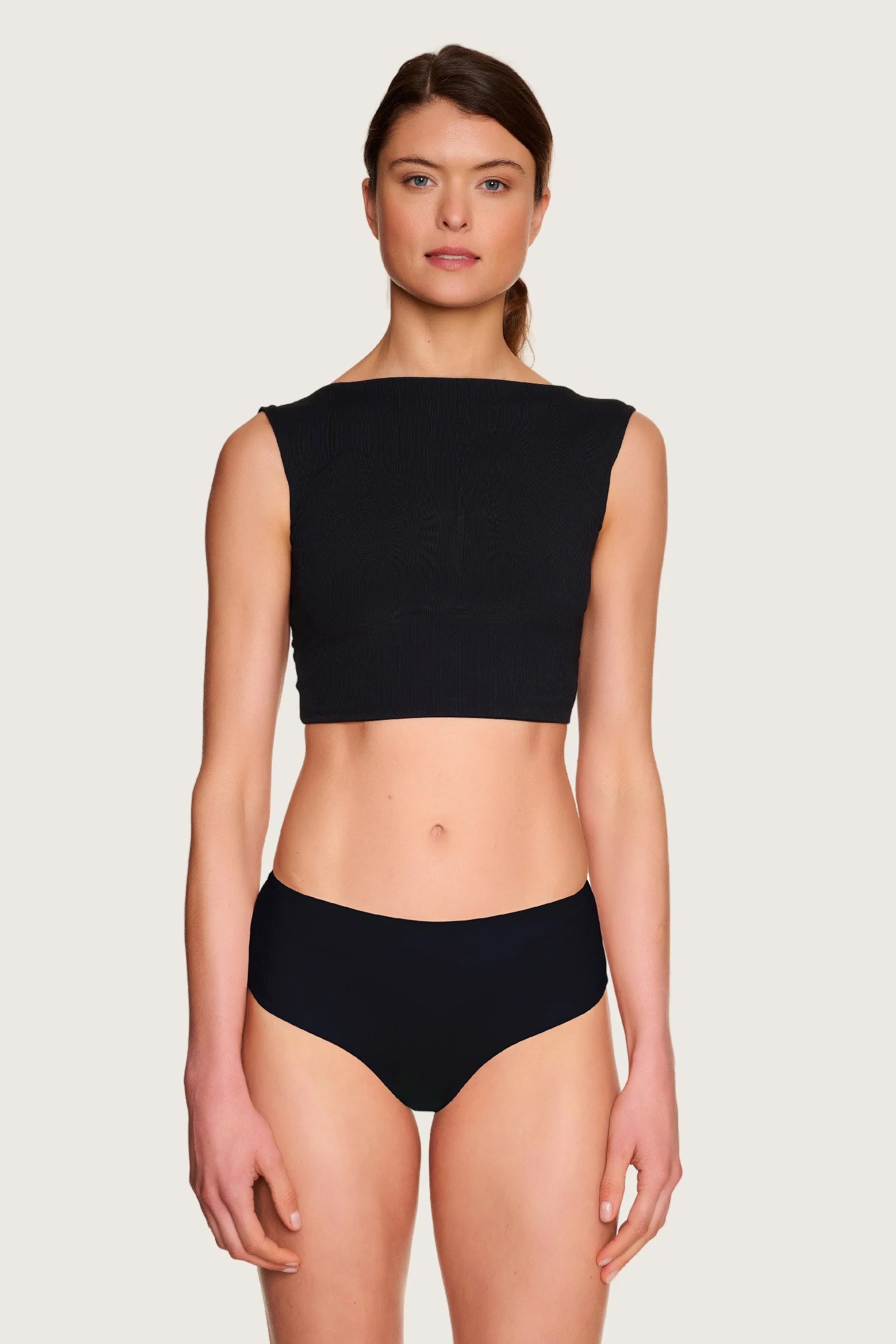 Frau trägt MYMARINI Bikinihose mit hohem Beinausschnitt und Top mit breiten Trägern vor neutralem Hintergrund.#color_black