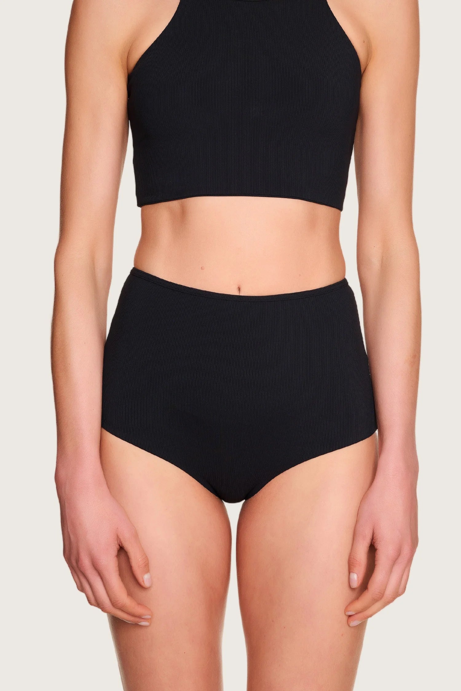 Person trägt MYMARINI Bikinihose mit hohem Bund und hochgeschlossenem Bikinitop in Schwarz.#color_black