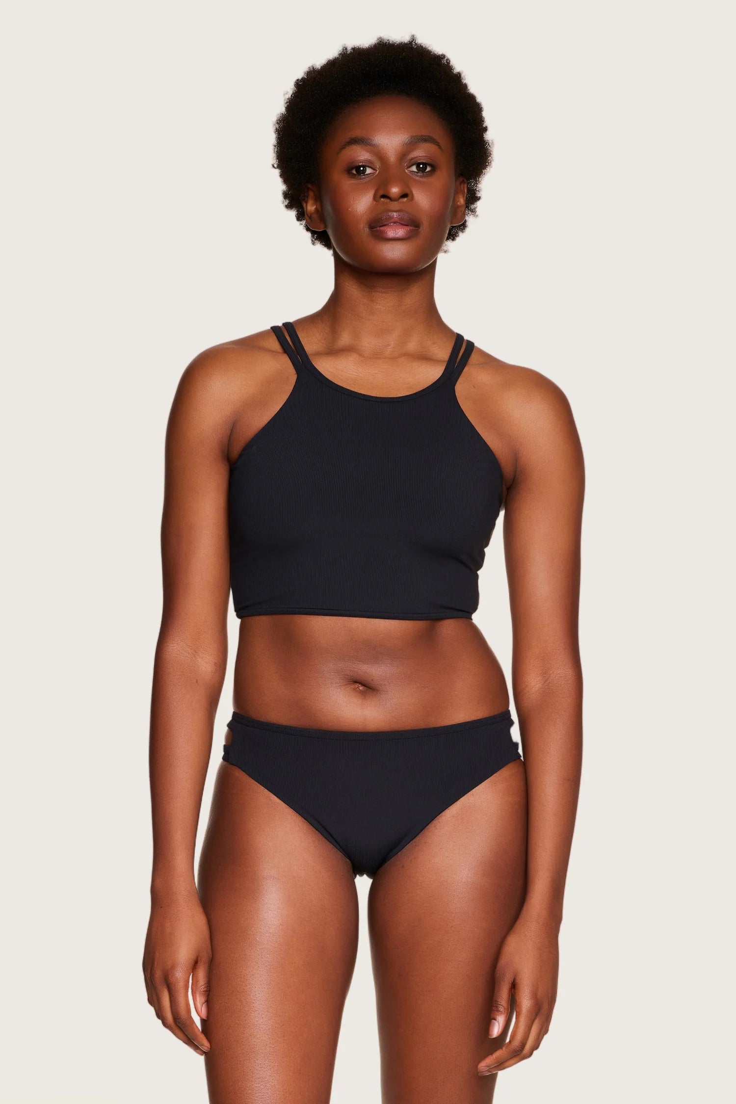 Frau trägt schwarzen MYMARINI Bikini mit hochgeschlossenem Top und Mid-Rise-Hose vor hellem Hintergrund.#color_black
