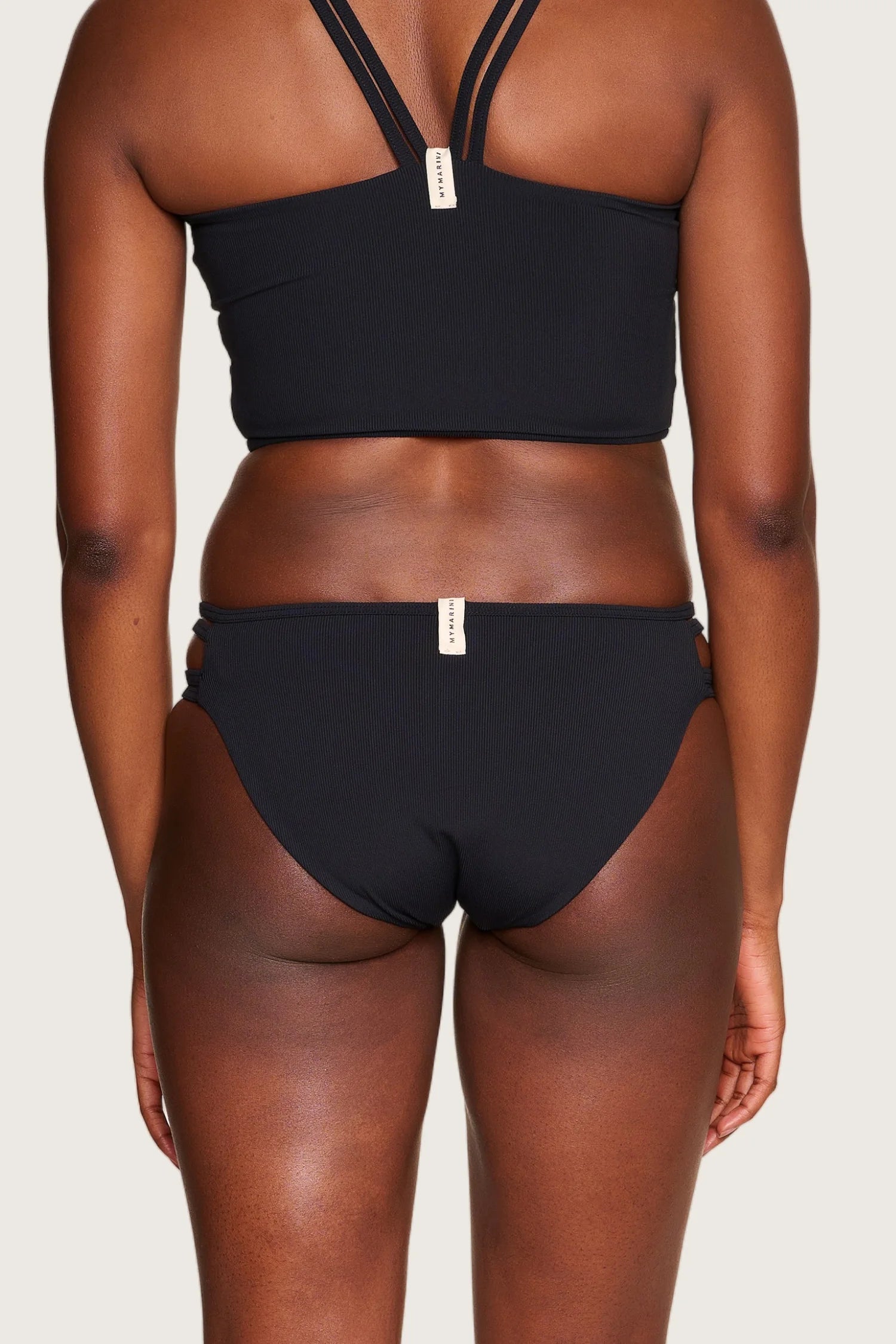 Rückansicht einer Person in schwarzem MYMARINI-Bikini mit breiten Trägern und hohem Beinausschnitt.#color_black