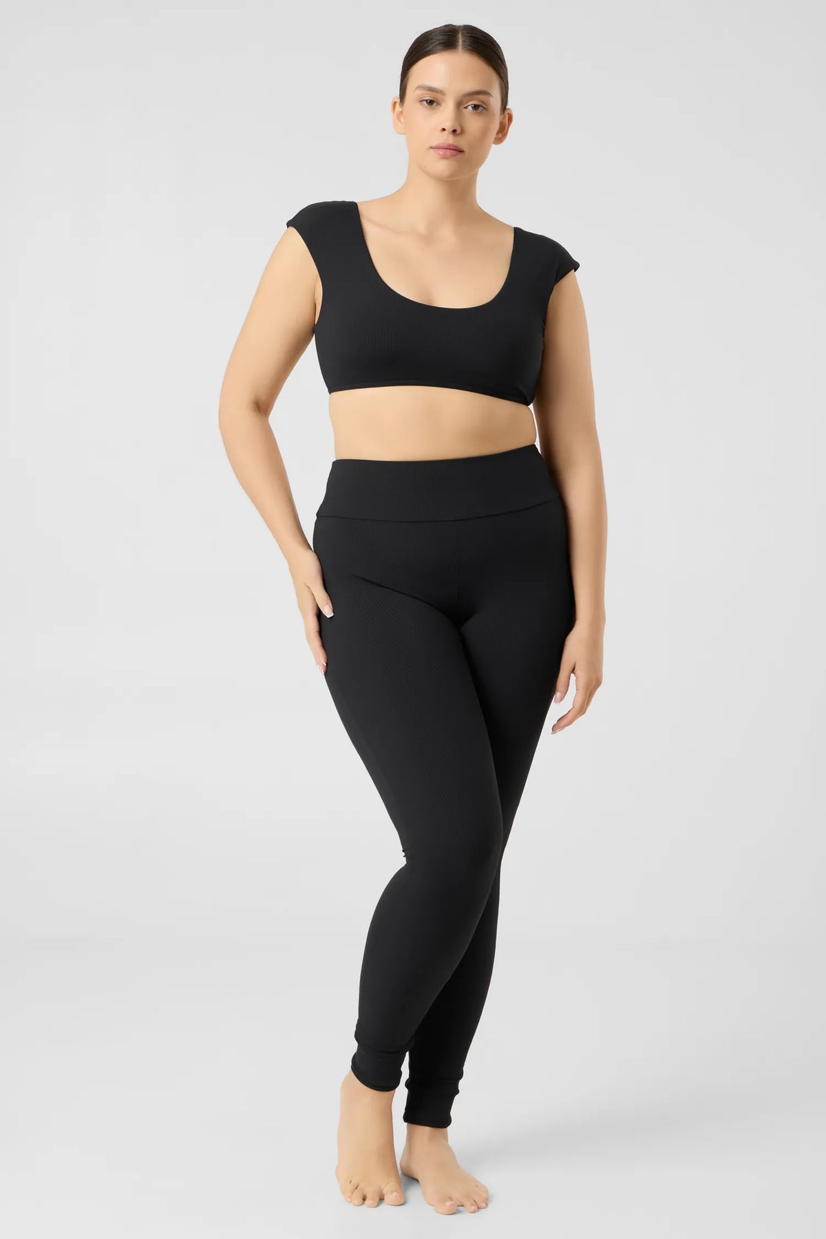 Woman in the black MYMARINI ALLDAY LEGGINGS with a high waistband and a black bikini top, front view#color_black-ribbed