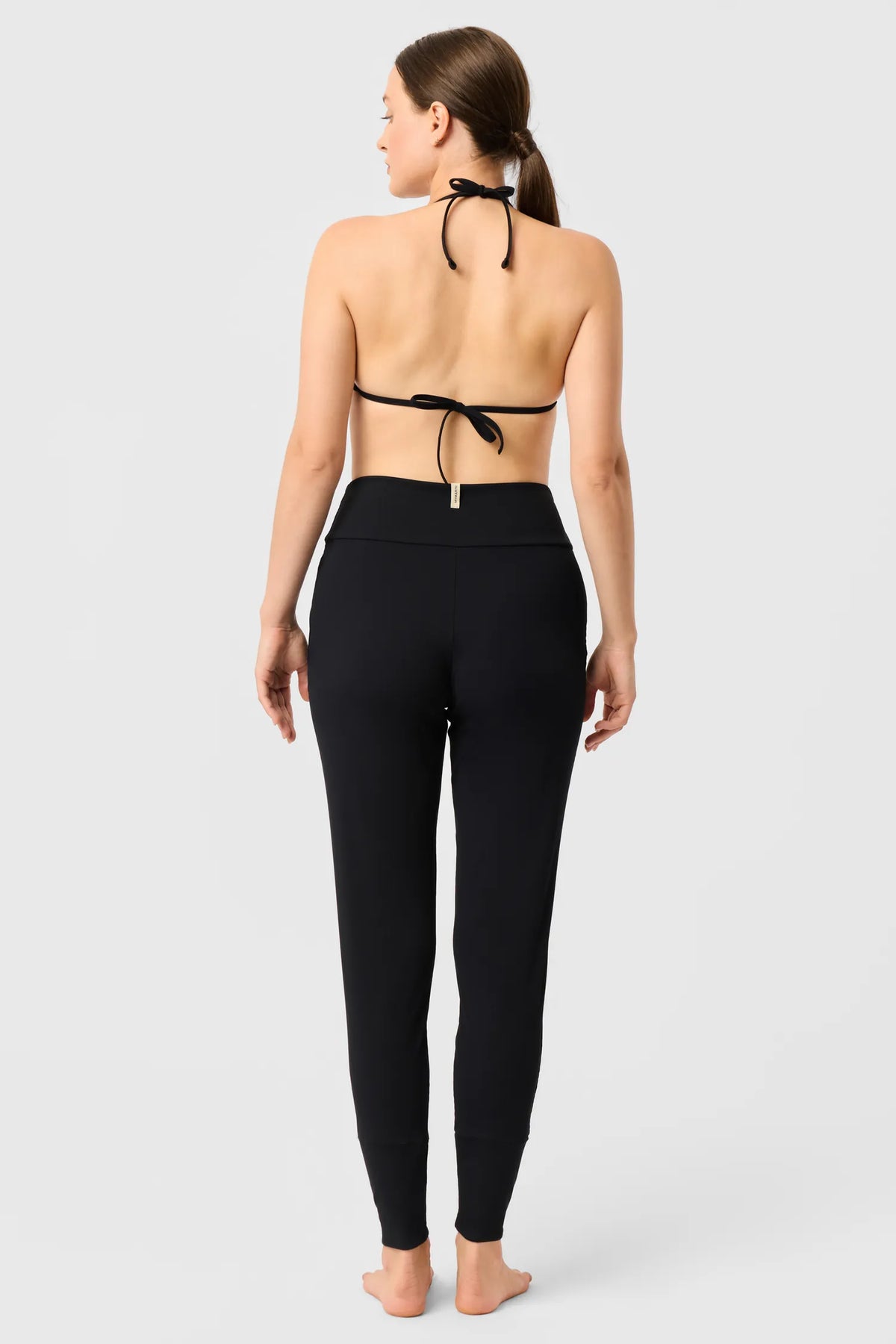 Rückansicht einer Frau in den schwarzen MYMARINI LOOSE LEGGINGS mit schwarzem Neckholder-Bikinitop#color_black-ribbed