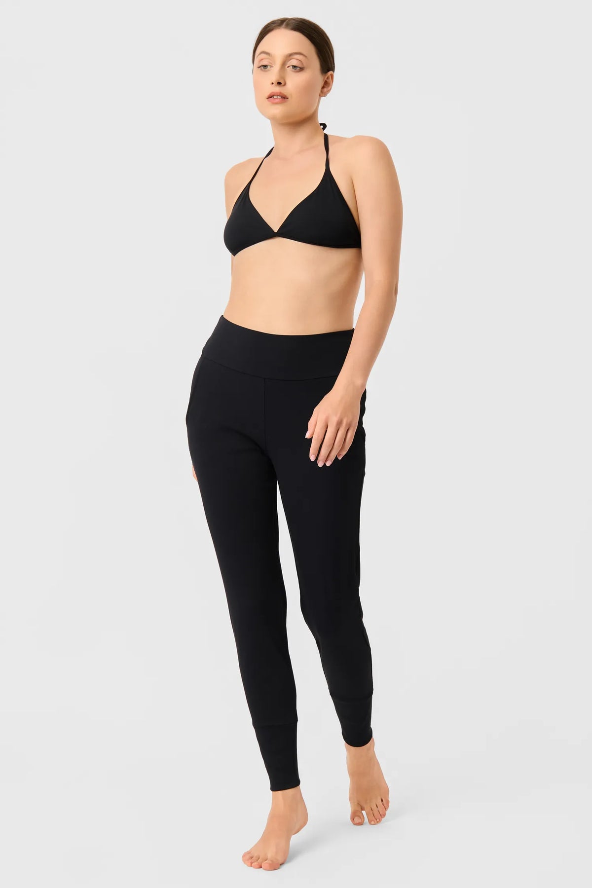 Frau in den schwarzen MYMARINI LOOSE LEGGINGS mit schwarzem Neckholder-Bikinitop, Vorderansicht#color_black-ribbed