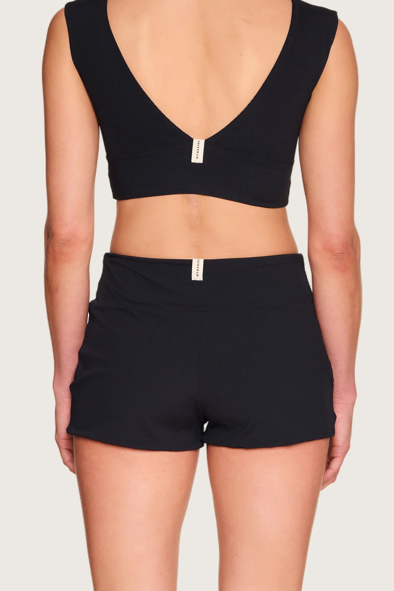 Rückansicht einer Person in schwarzem MYMARINI Bikinitop mit V-Ausschnitt und Shorts.#color_black