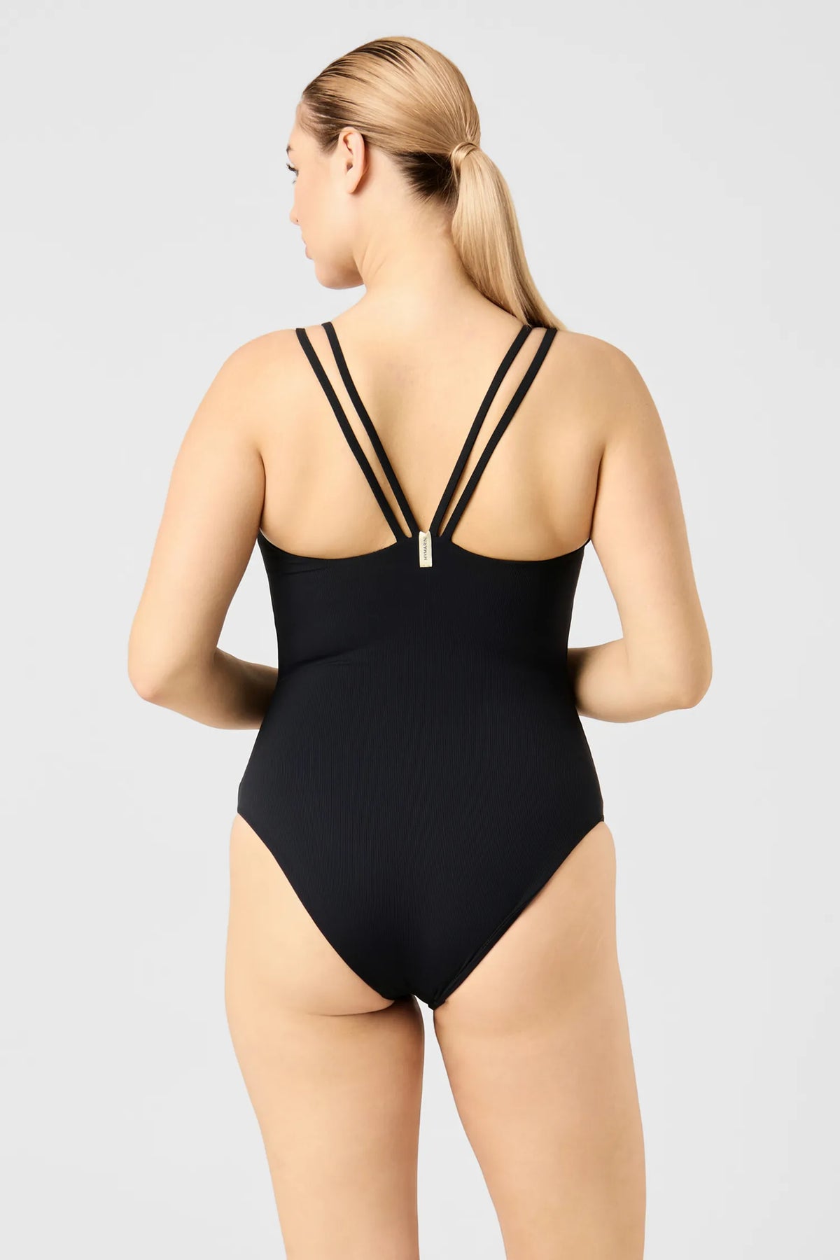 Back view of a woman in the black MYMARINI CLEANSUIT swimsuit, double straps meeting in a V#color_black-ribbed