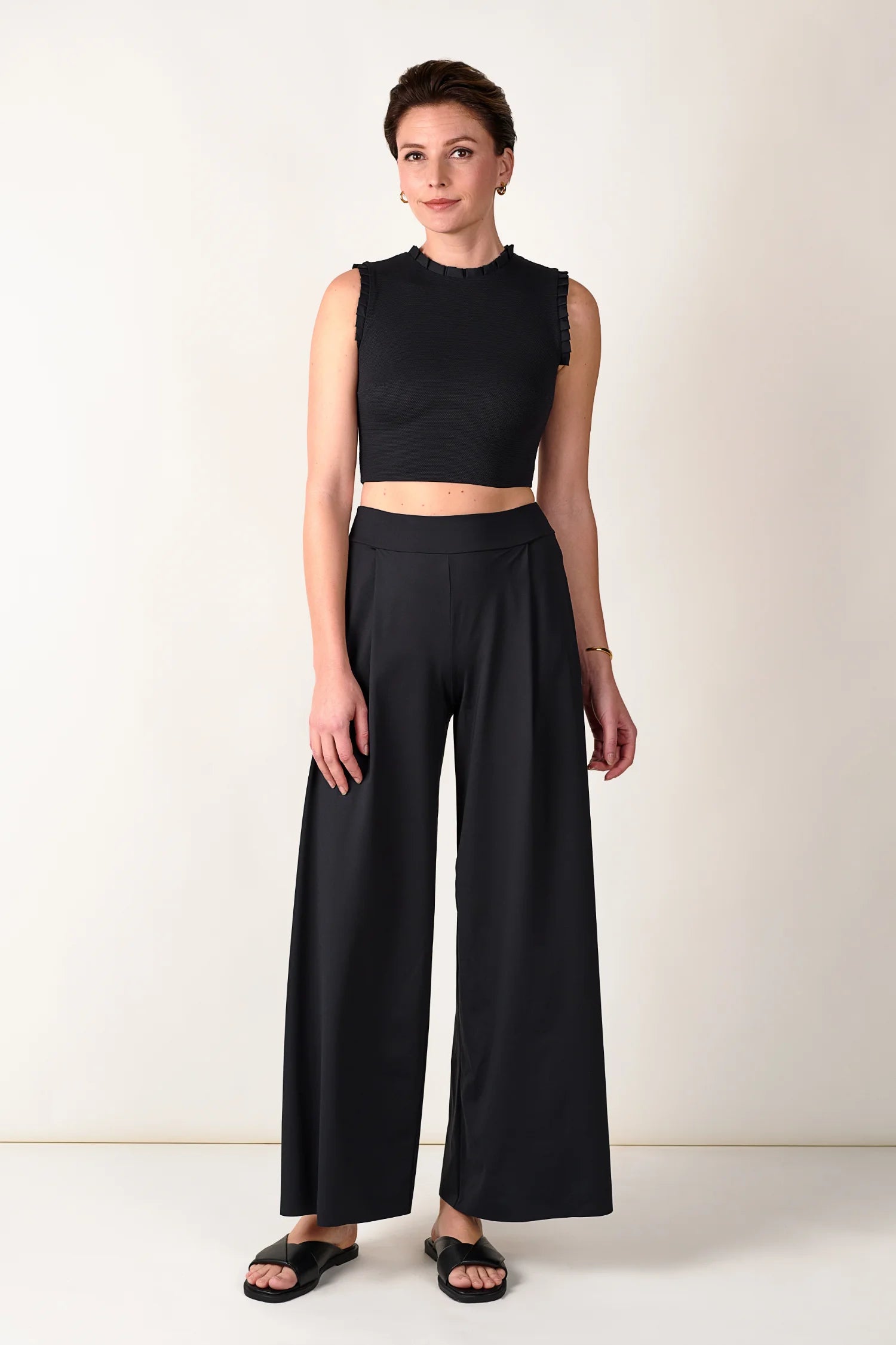 Frau trägt schwarzes MYMARINI Top mit Rundhalsausschnitt und weite Hose, stehend vor hellem Hintergrund.#color_black