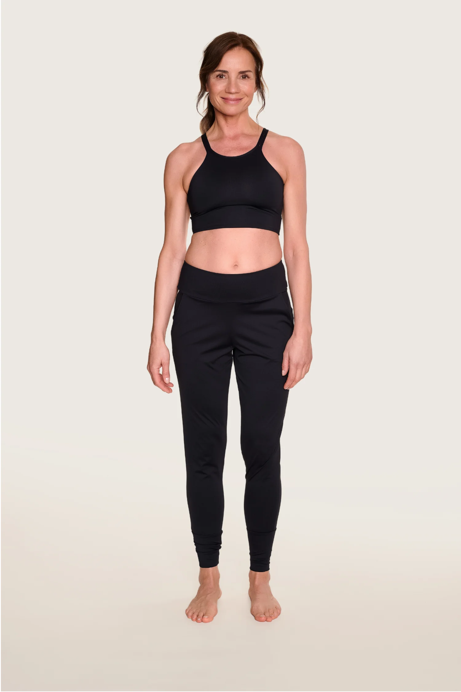 Frau in schwarzem MYMARINI-Top mit breiten Trägern und passender Hose, lächelnd vor hellem Hintergrund.#color_black