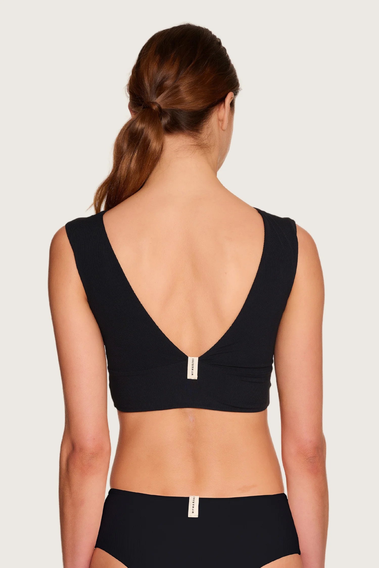 Frau in MYMARINI Bikinitop mit tiefem Rückenausschnitt und breiten Trägern, dazu passende Bikinihose.#color_black