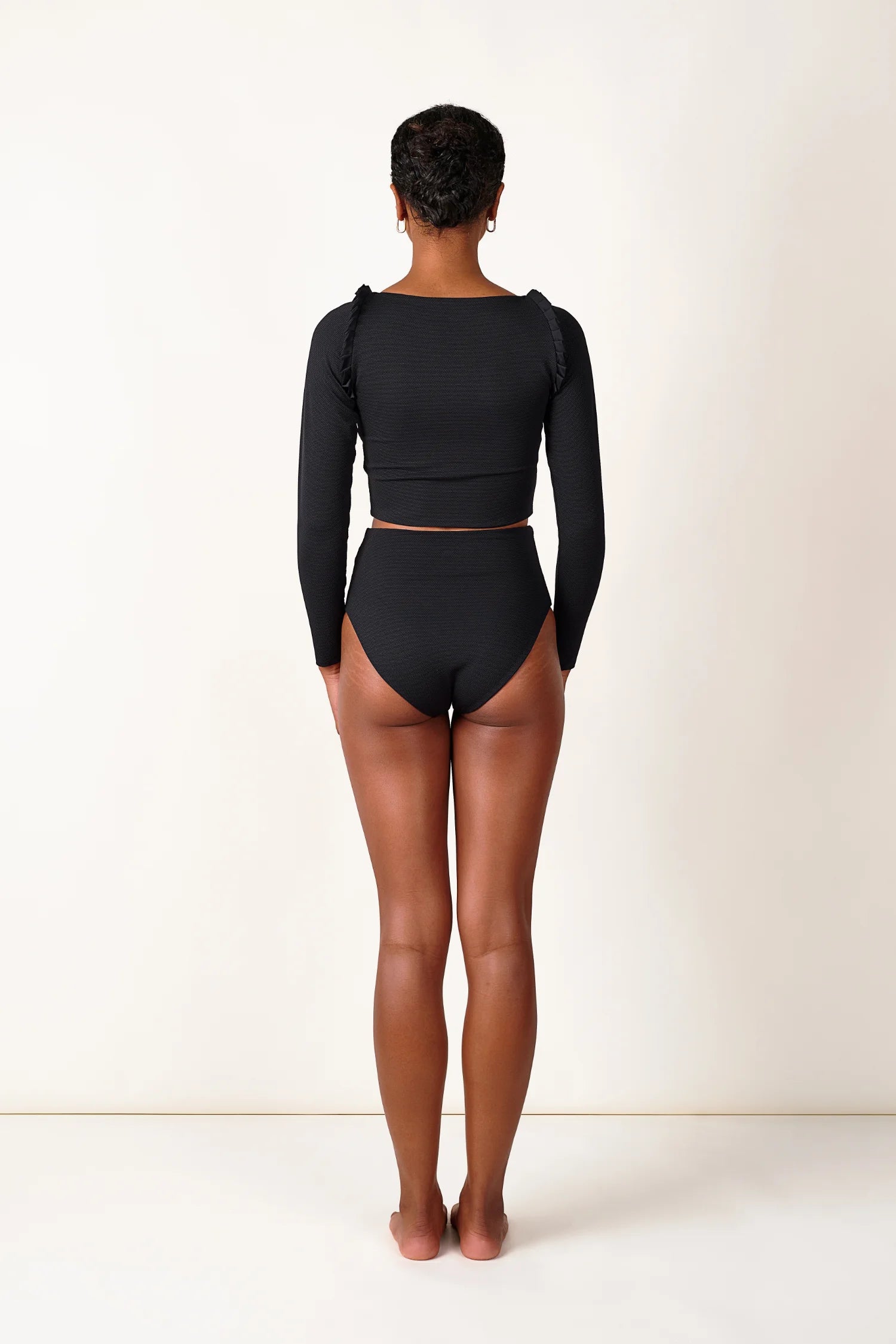 Person trägt schwarzen MYMARINI-Bikini mit langärmligem Top und hoch geschnittener Bikinihose, von hinten gesehen.#color_black