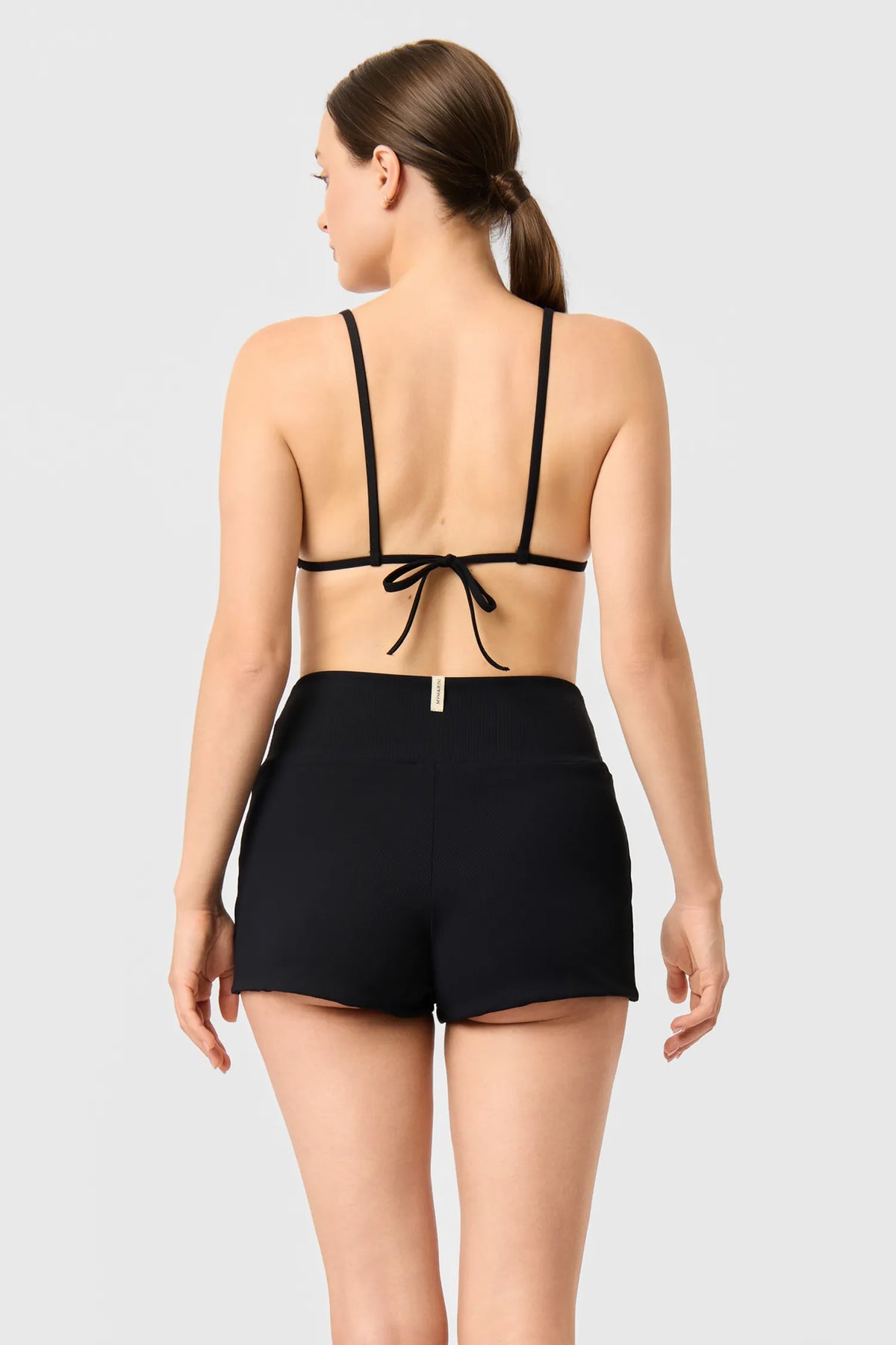 Back view of a woman in the black MYMARINI TRIANGLE TOP bikini top tied at the back, with black shorts#color_black-ribbed