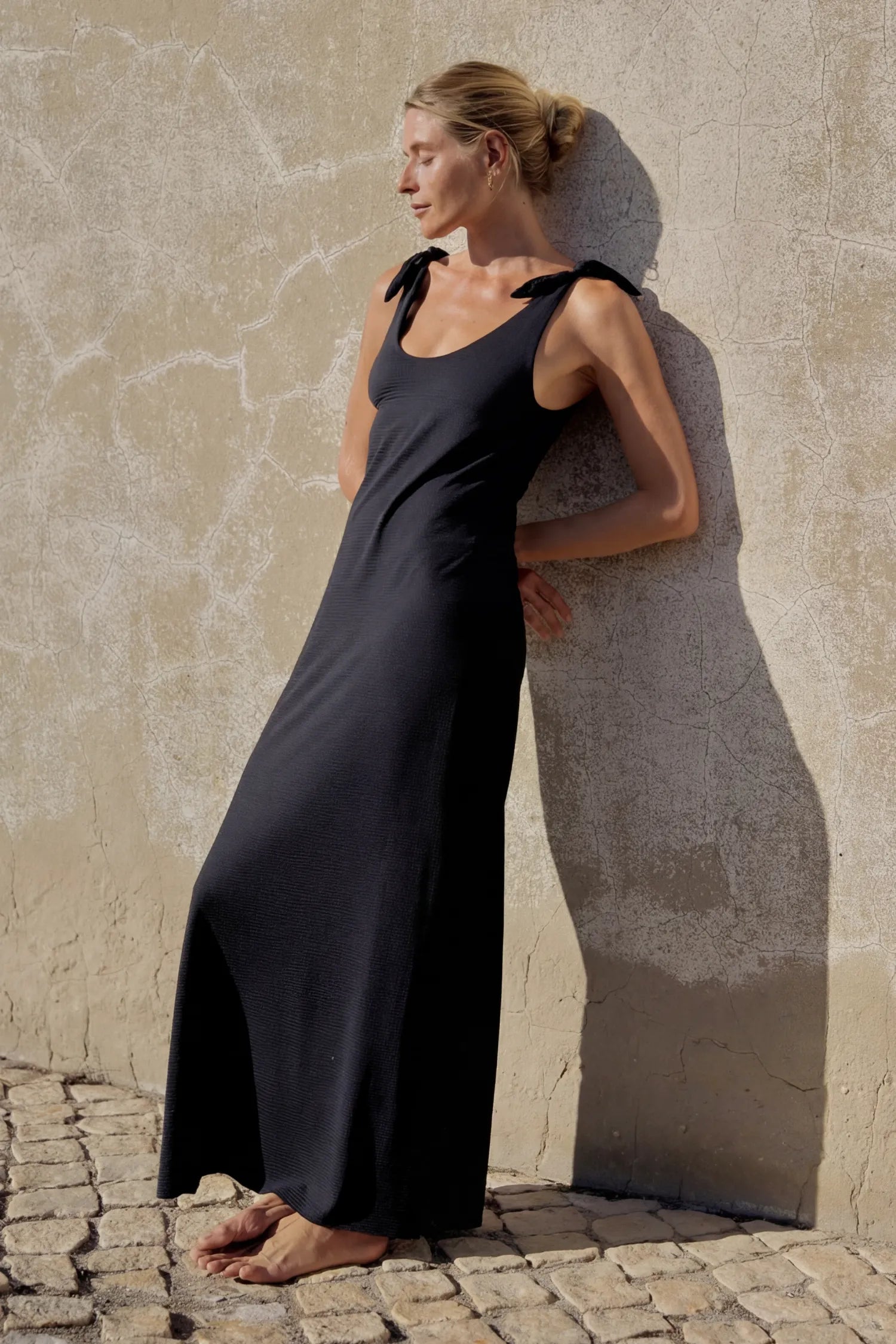 MYMARINI One-Piece-Badeanzug, schwarz: breiten Trägern mit Schleifen, lange Länge, Frau an Steinwand.