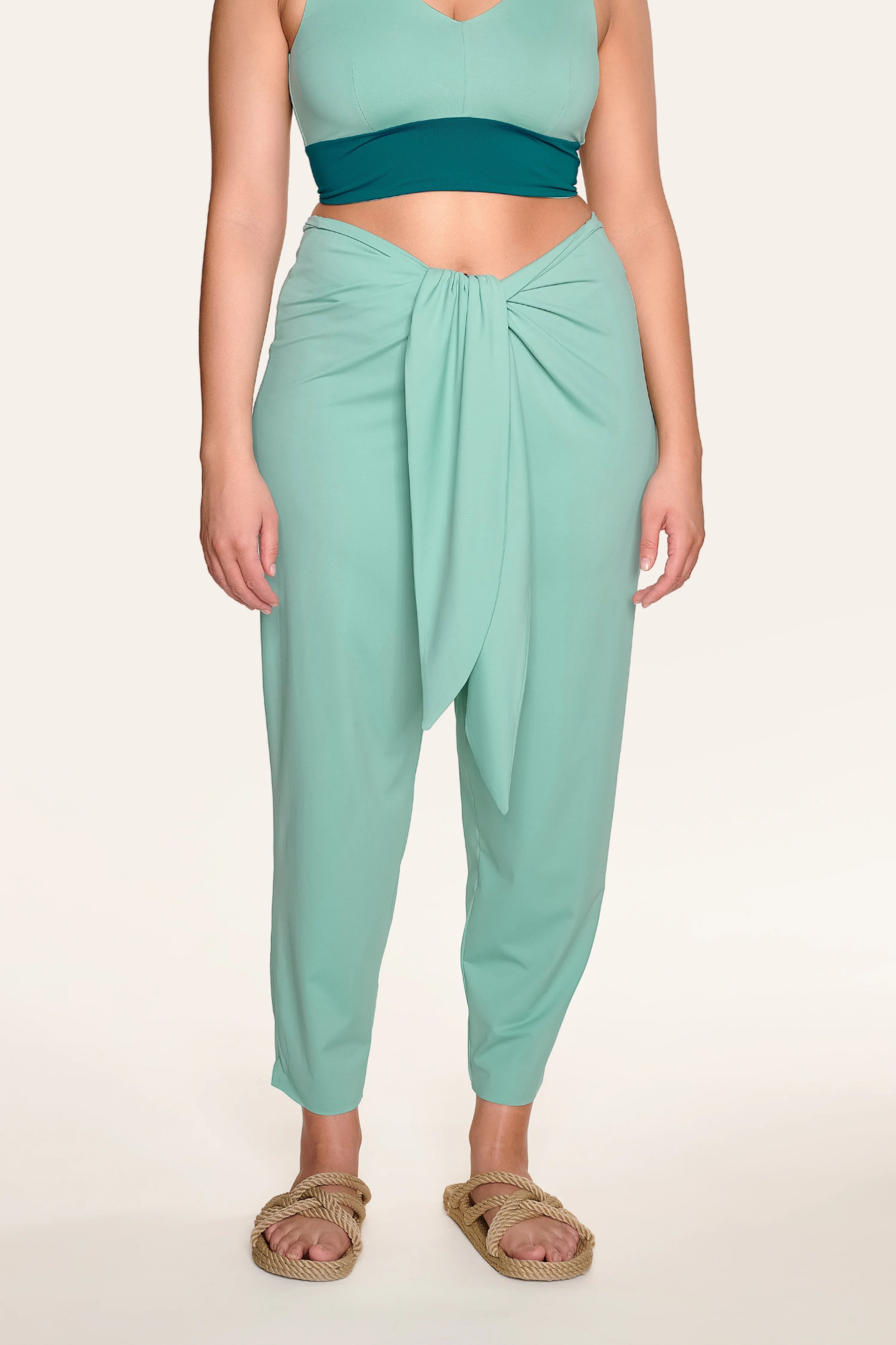 Person trägt MYMARINI-Hose in Mintgrün mit lockerem Schnitt, kombiniert mit einem türkisfarbenen Bikinitop.#color_eucalyptus