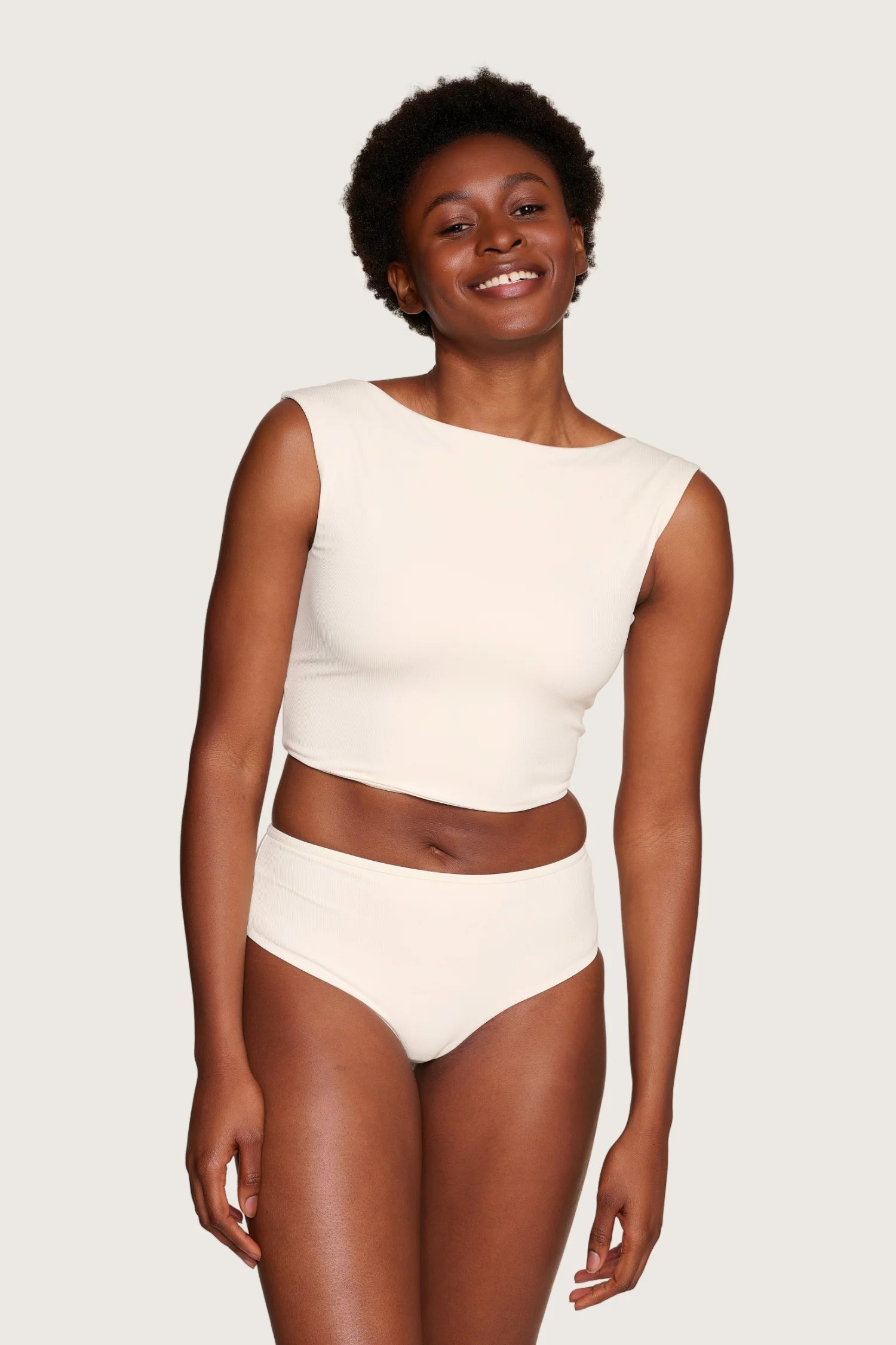 Lächelnde Person trägt MYMARINI Top mit breiten Trägern und Bikinihose in Creme, hochgeschlossen, vor neutralem Hintergrund.#color_off-white