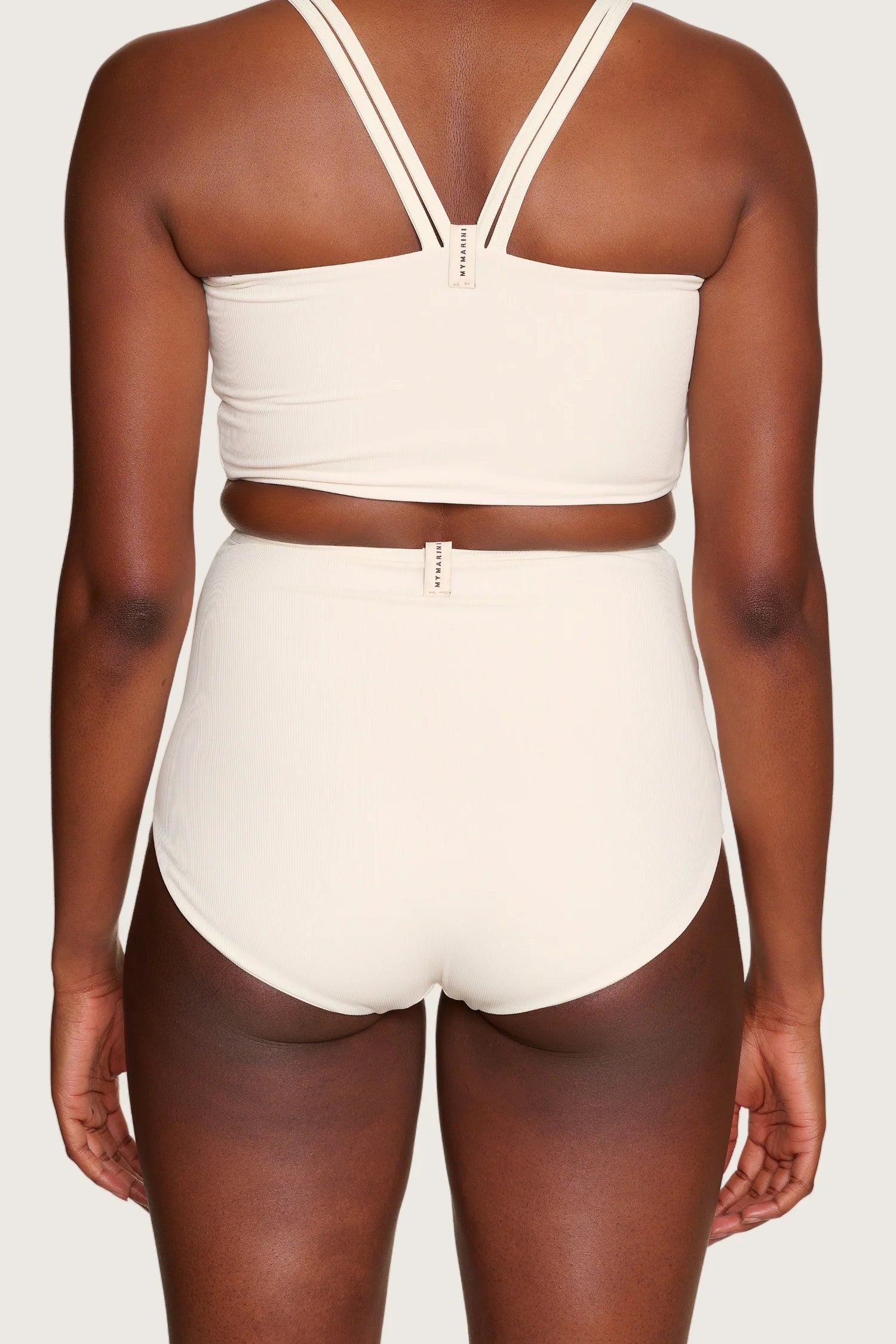 Rückansicht einer Person in cremefarbenem MYMARINI-Bikinitop mit breiten Trägern und High-Waist-Bikinihose.#color_off-white