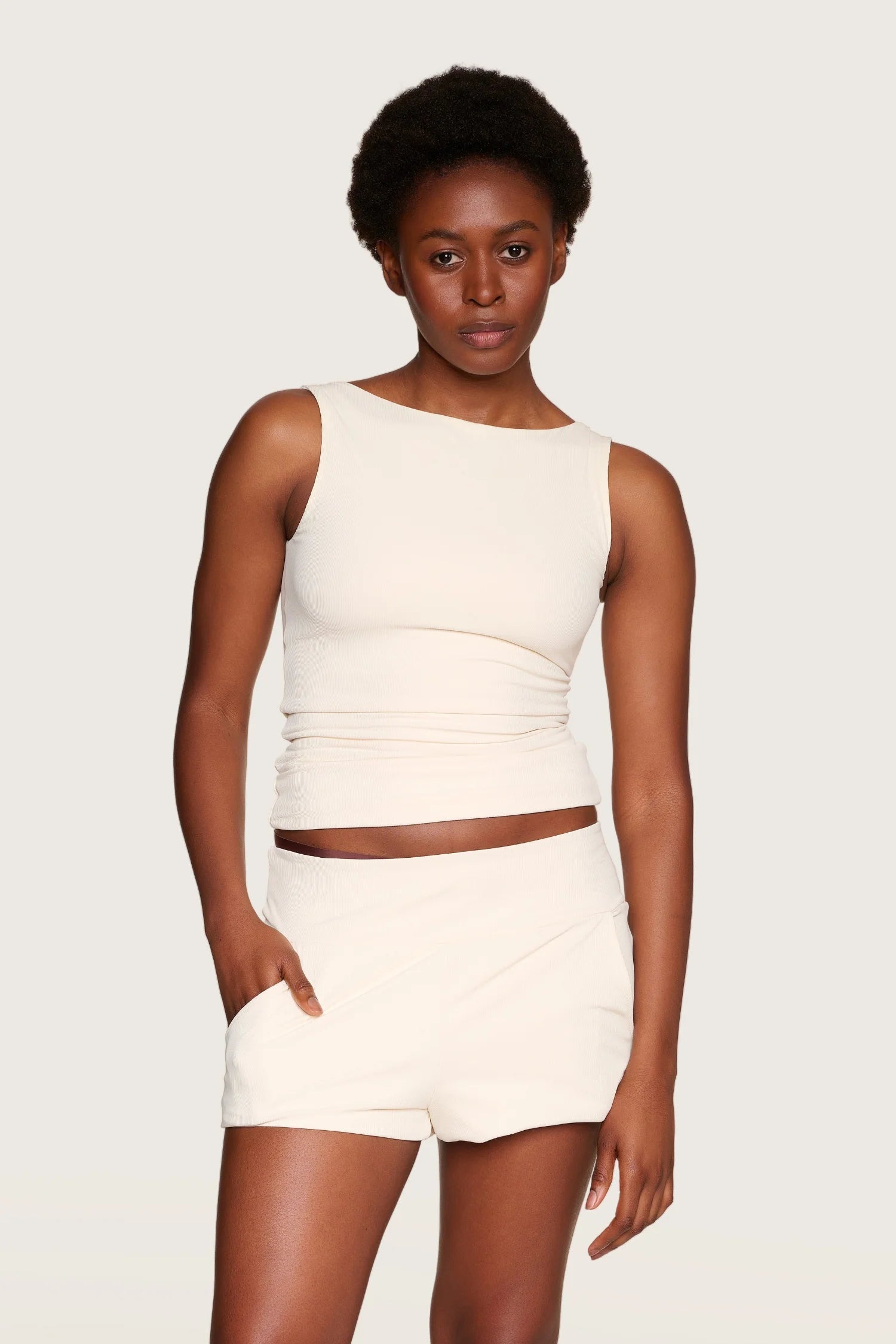 Person trägt MYMARINI Top mit breiten Trägern und Shorts in Cremeweiß, stehend vor neutralem Hintergrund.#color_off-white
