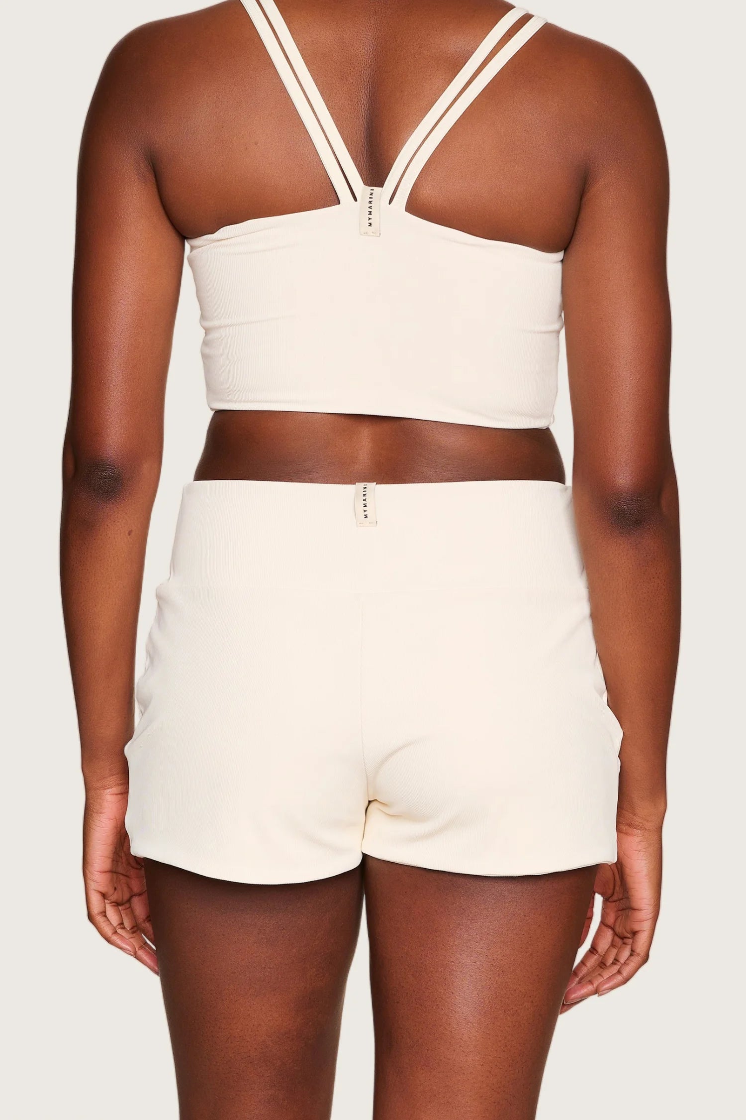 Rückansicht einer Person in MYMARINI Bikinitop mit breiten Trägern und Shorts in Cremeweiß.#color_off-white