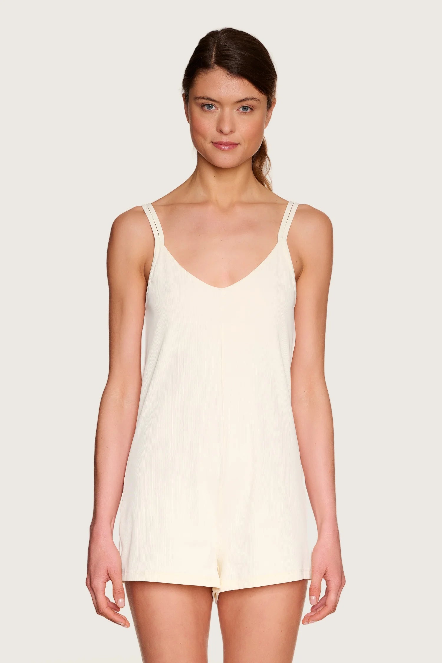 Frau trägt MYMARINI Jumpsuit mit V-Ausschnitt und Spaghettiträgern in Cremefarbe, vor neutralem Hintergrund.#color_off-white